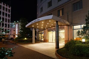 Entrada de un hotel con un corredor cubierto, un letrero con caracteres japoneses y un edificio con amplias ventanas.