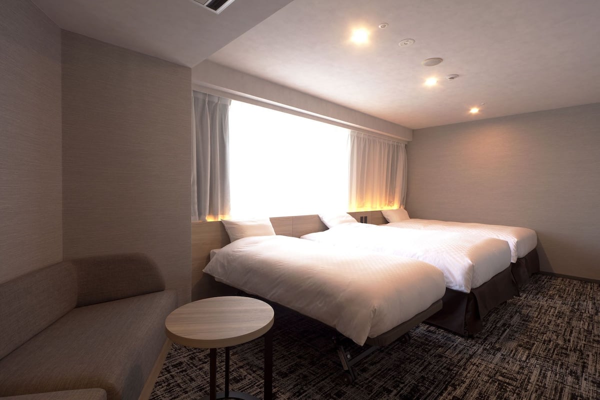 Ein Hotelzimmer mit zwei Betten, einem kleinen runden Tisch und einer Couch.