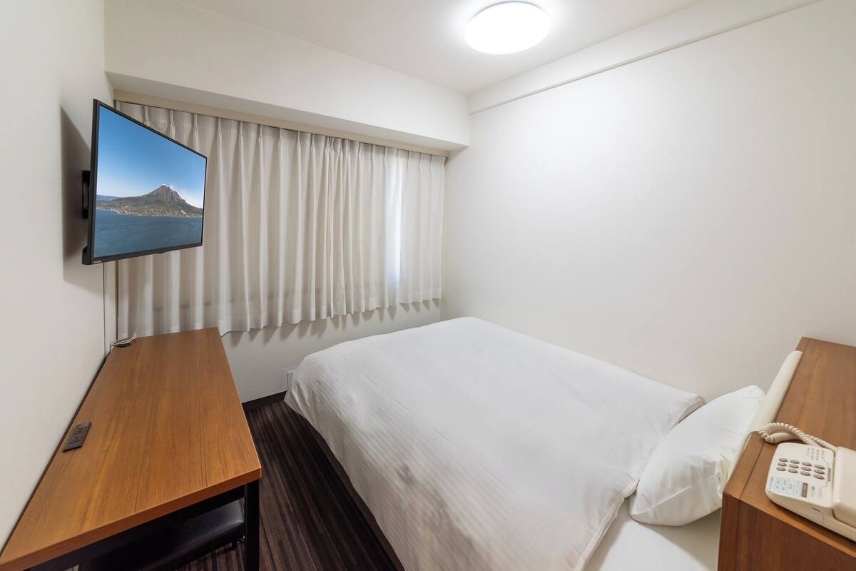 Une chambre d’hôtel équipée d’un lit, d’un bureau, d’un téléviseur fixé au mur et d’un téléphone sur le bureau.