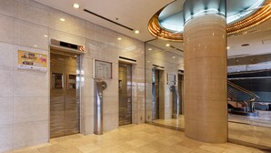 Un hall d’entrée moderne avec des ascenseurs, une grande colonne et un escalier.