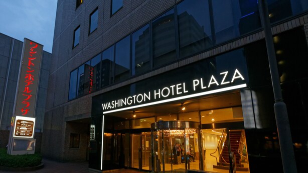 L’extérieur du Washington Hotel Plaza se distingue par sa façade moderne en verre, son entrée avec porte tournante et un escalier apparent menant au hall d’entrée.