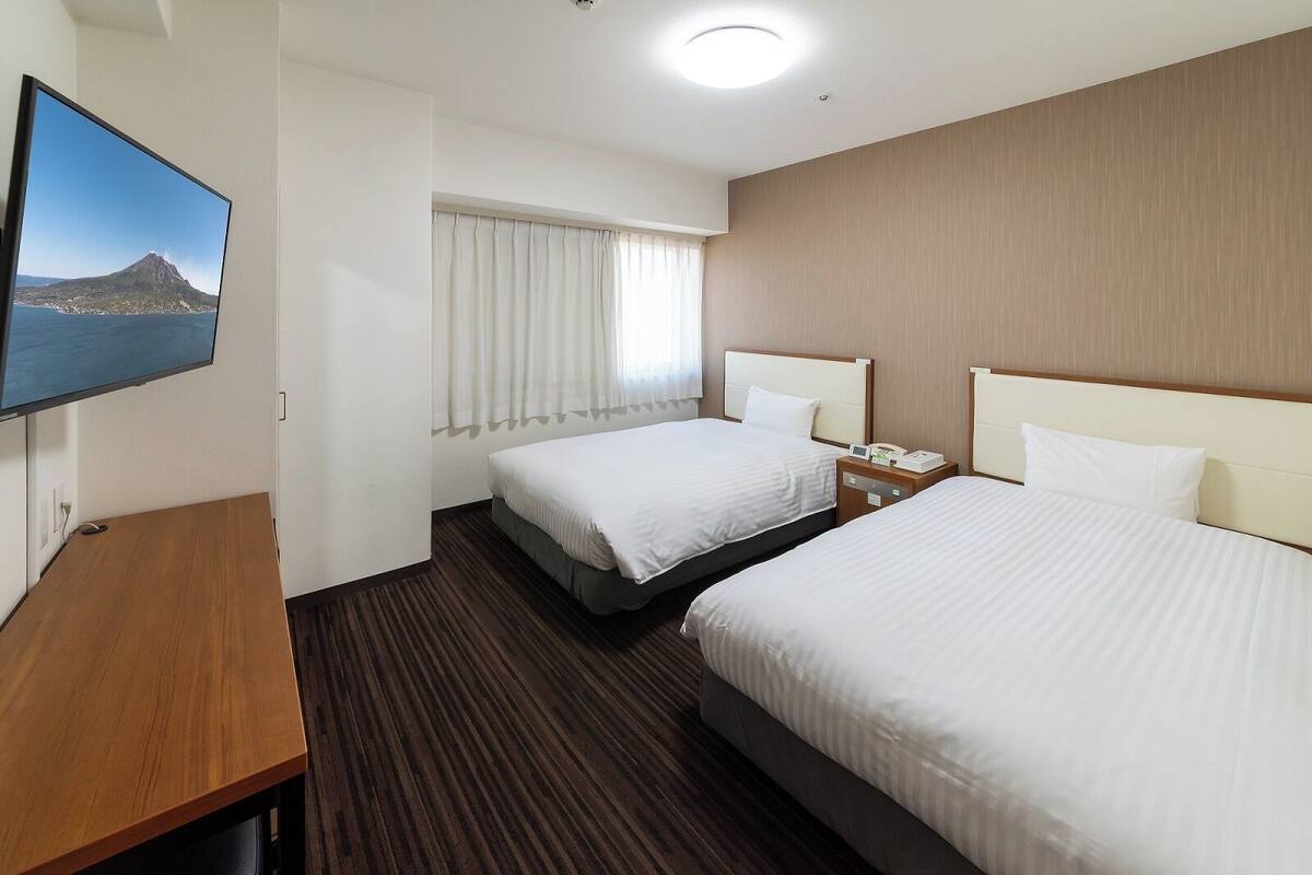 Une chambre d’hôtel avec deux lits, une télévision, un bureau et une fenêtre avec des rideaux.