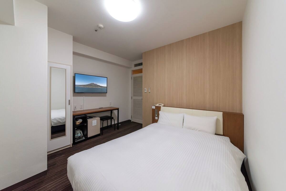 Une chambre d’hôtel avec un lit, un bureau, une télévision et un miroir.