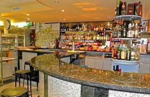 A bar area with a granite countertop, shelves stocked with bottles, and a clock on the wall. - Hotel Vilobí (Vilobi d'Onyar)