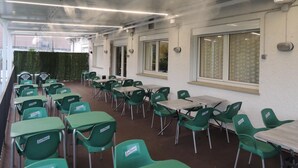 A spacious indoor area with rows of green chairs and tables, large windows, and a high ceiling with exposed beams. - Hotel Vilobí (Vilobi d'Onyar)