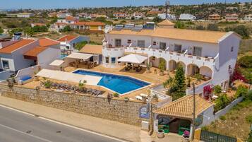 A villa with a swimming pool, outdoor seating, and a view of the surrounding neighborhood.