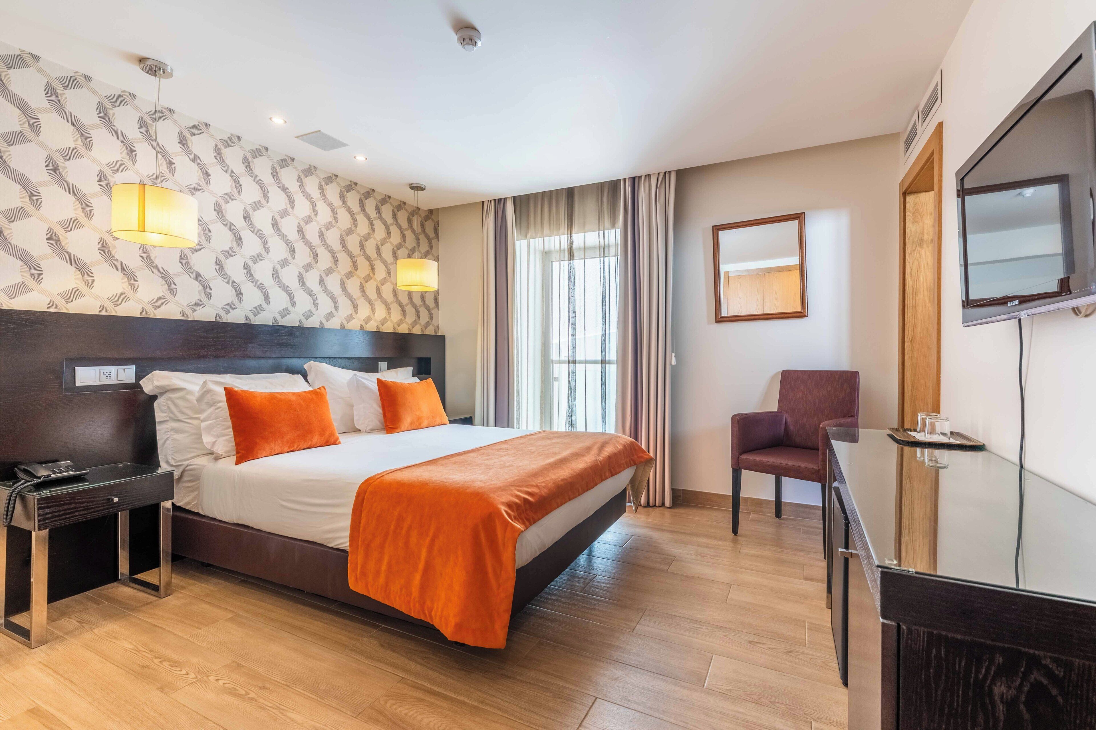 Una camera d'albergo con un letto grande, una scrivania, una sedia, una televisione e una finestra con tende.