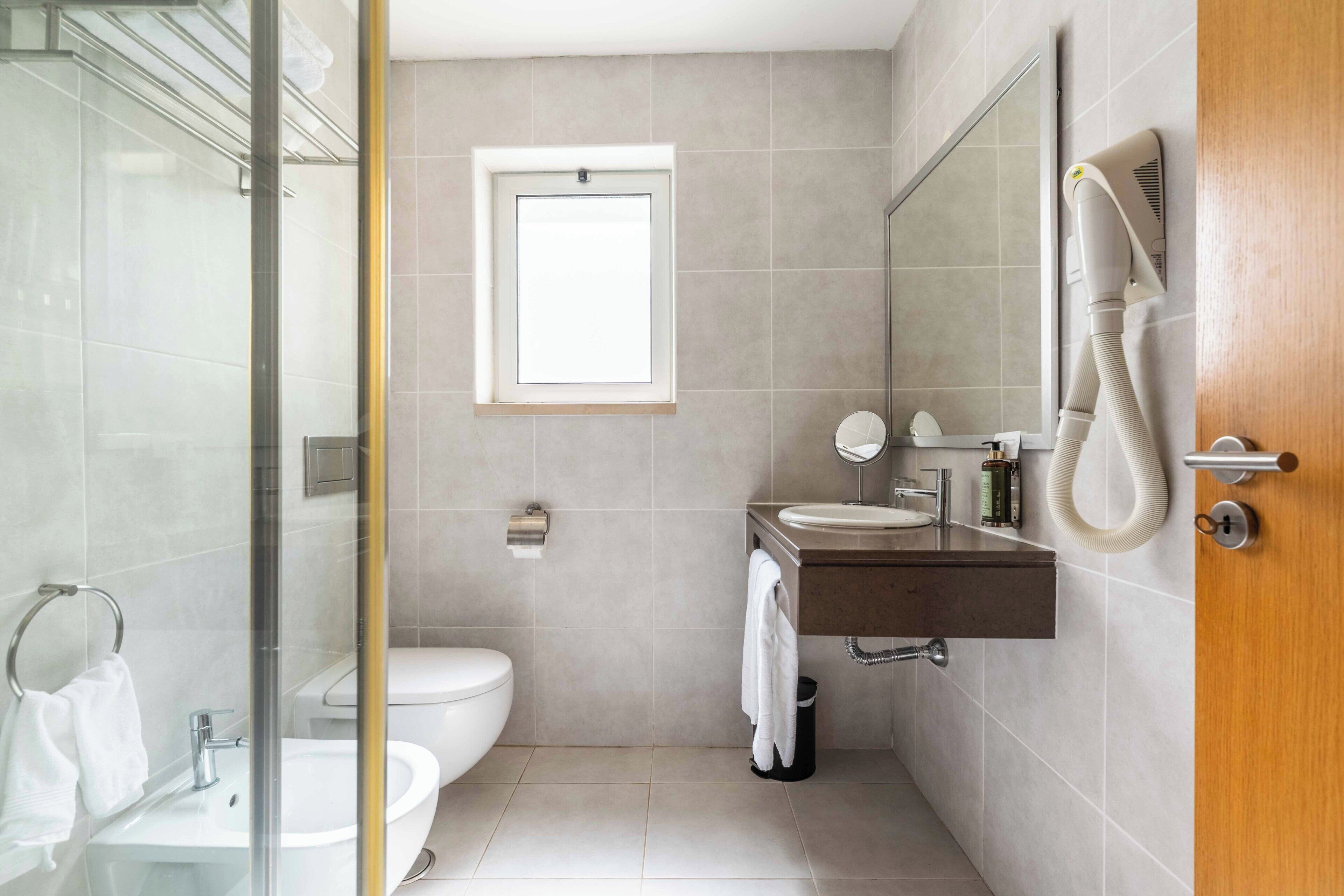 Un bagno moderno con cabina doccia in vetro, un water, un lavandino con specchio e un porta asciugamani.