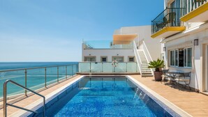 Zwembad met glazen balustrade, een trap naar een hoger gelegen terras en uitzicht op zee.