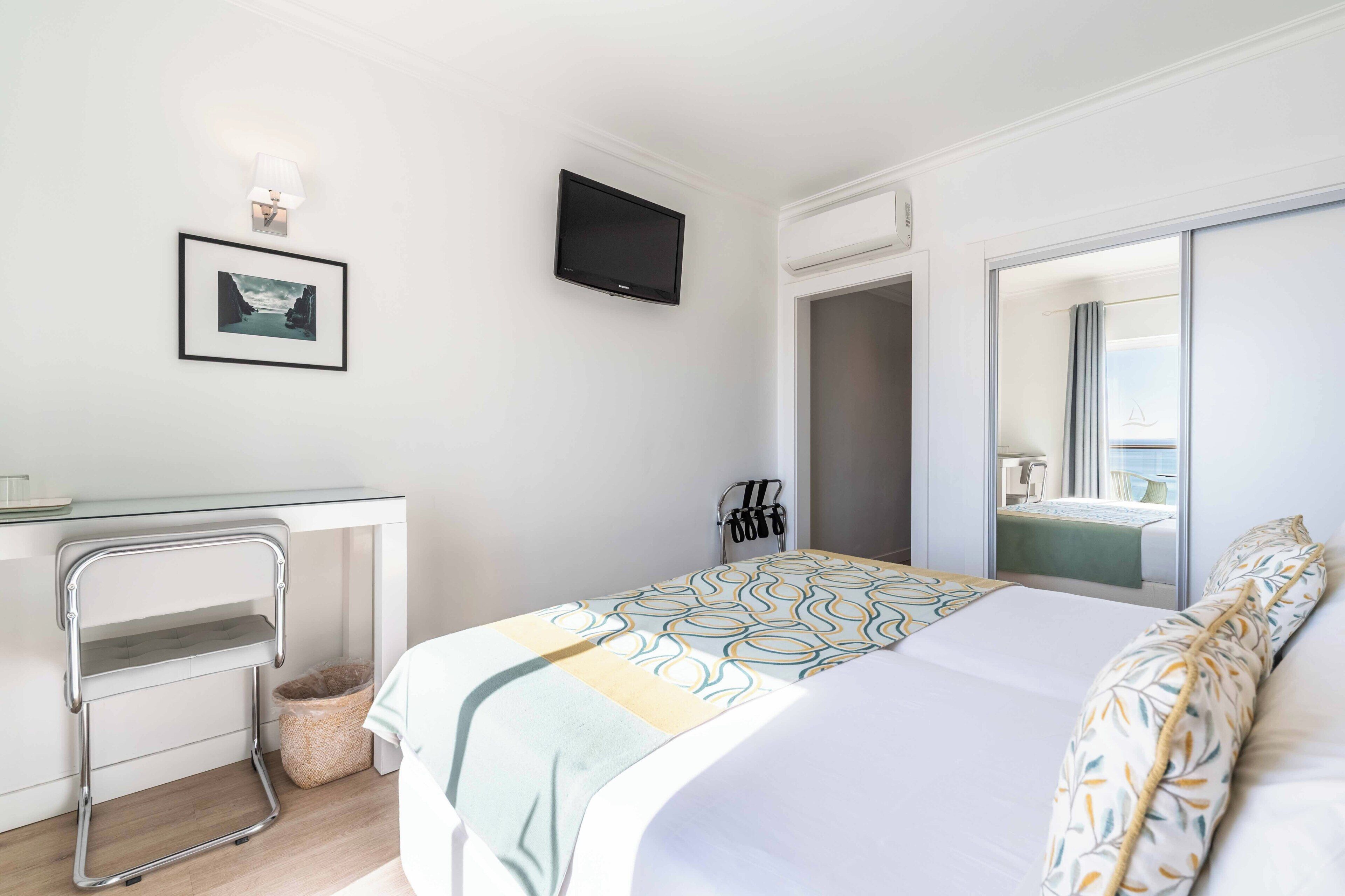 Habitación de hotel con cama, escritorio, televisor, espejo y ventana.