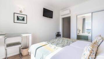 Habitación de hotel con cama, escritorio, televisor, espejo y ventana.