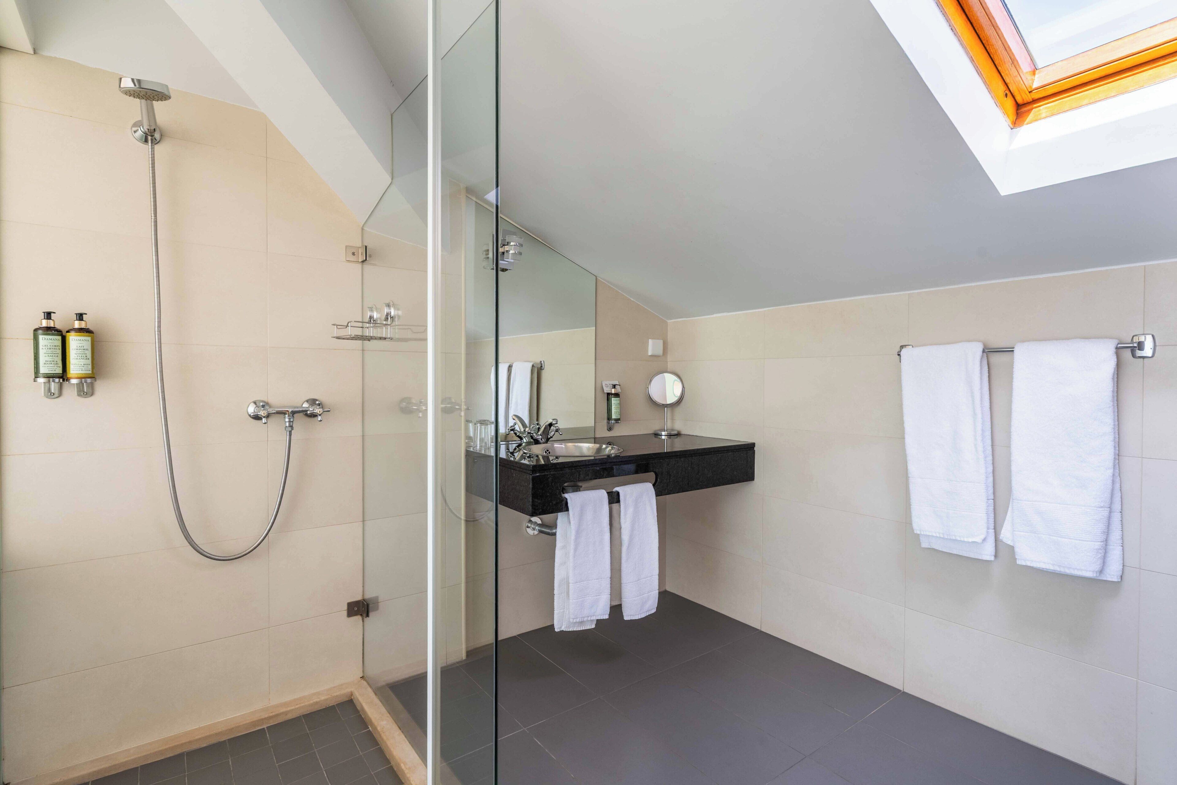 A modern bathroom with a glass-enclosed shower, a black countertop sink, and two white towels.