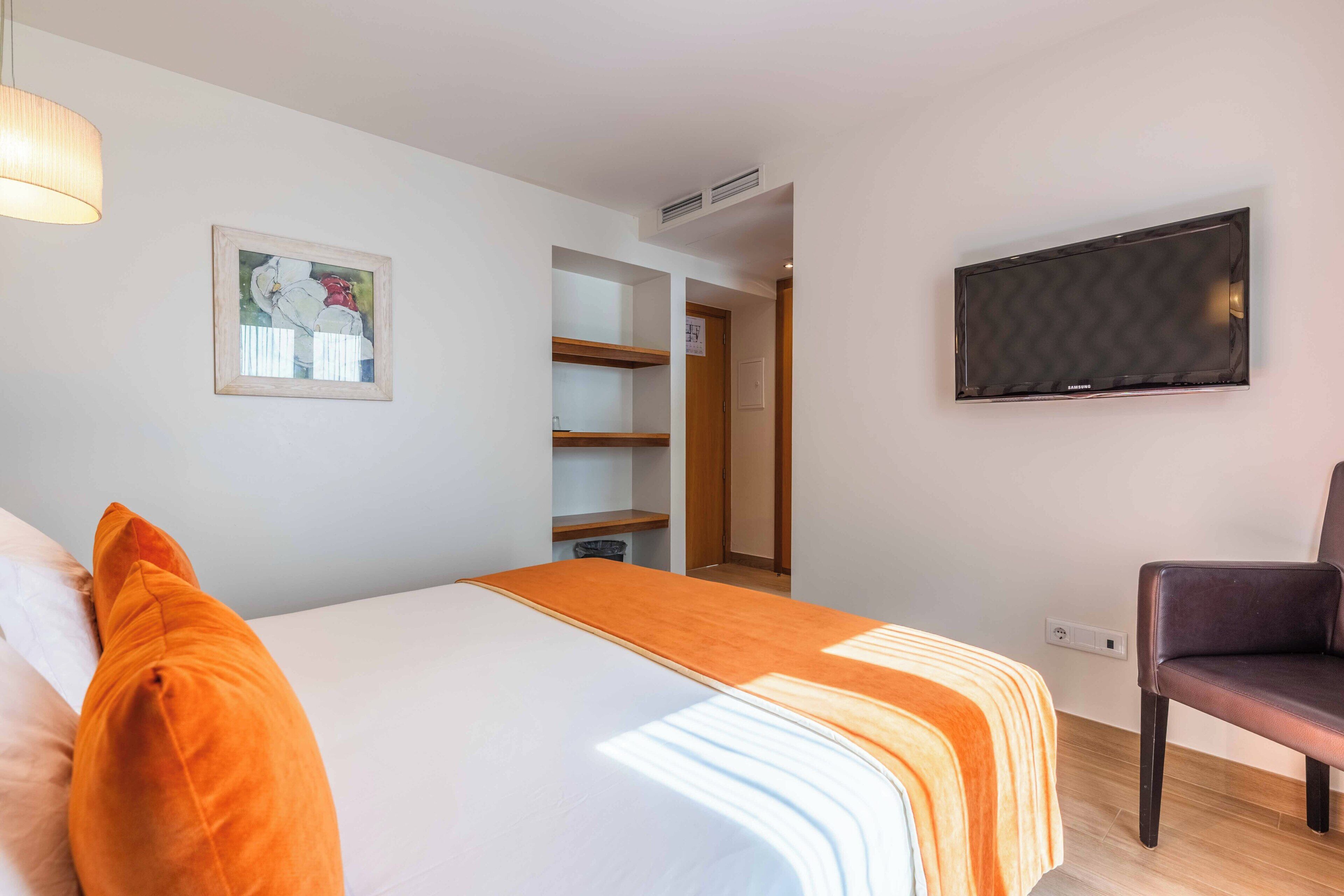Ein Hotelzimmer mit einem Bett, einem Sessel, einem Fernseher und einem Bild an der Wand.