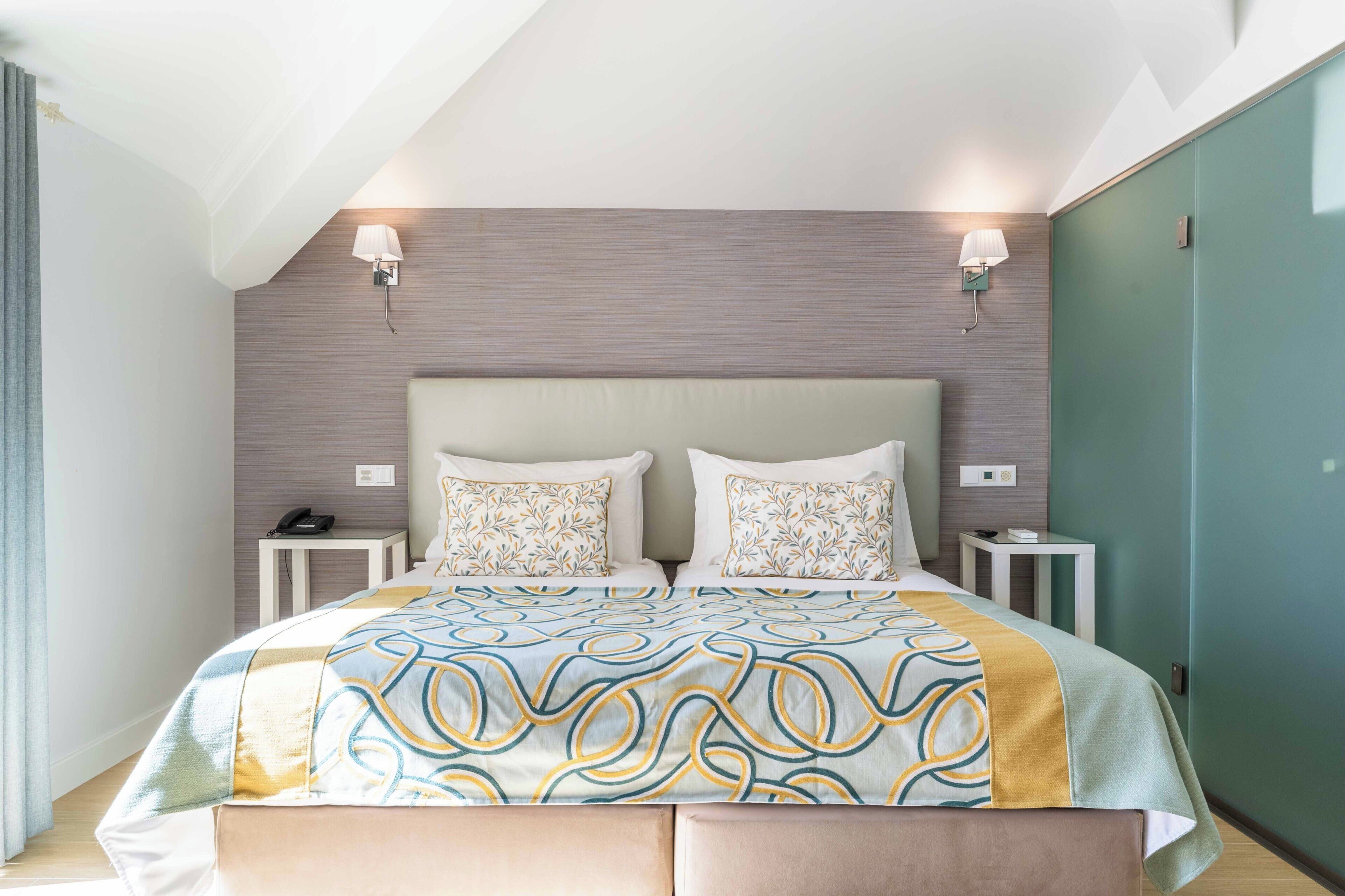 A hotel room with a large bed, two bedside tables, a headboard, and wall-mounted lamps.
