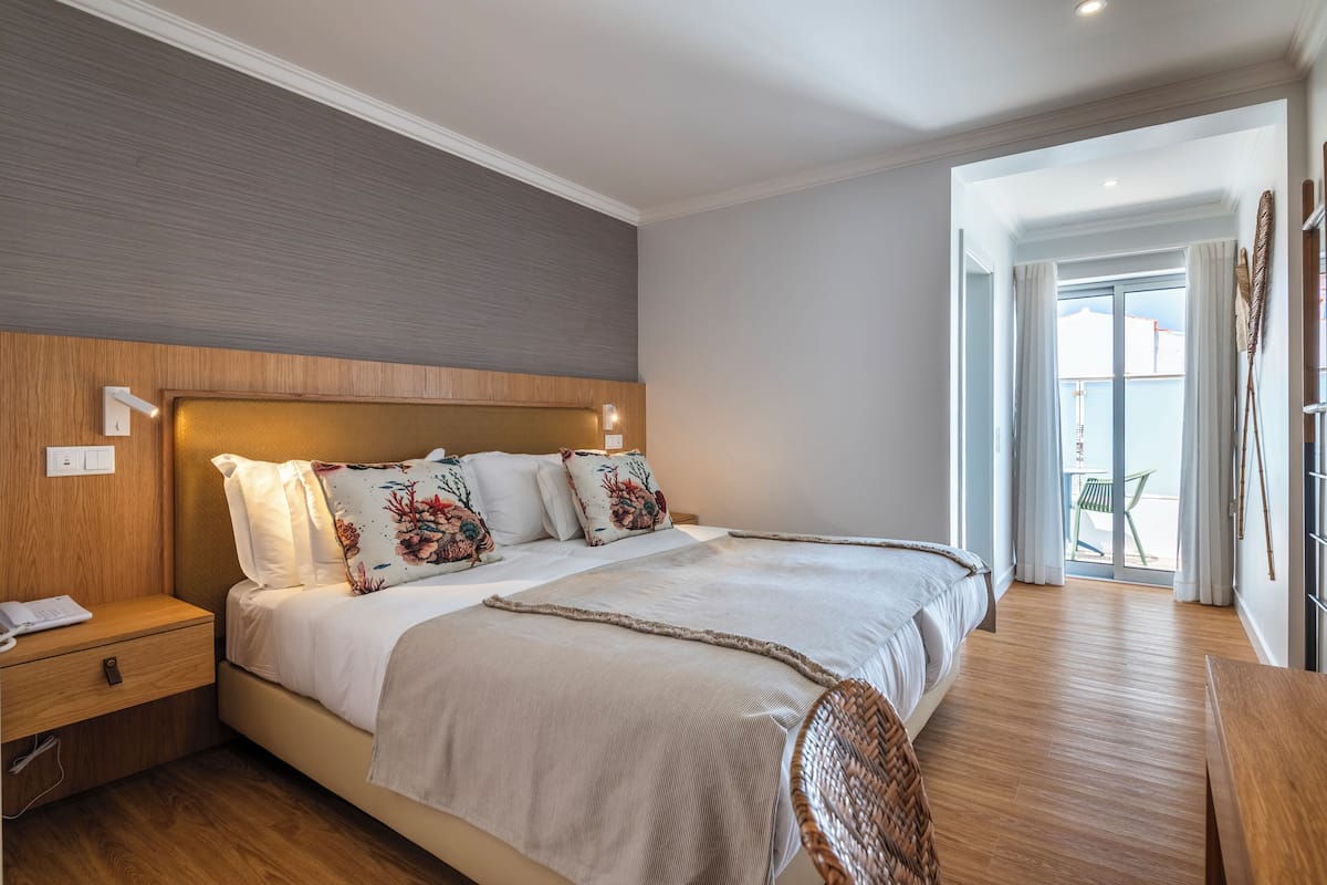 Une chambre avec un grand lit, une tête de lit en bois, une table de chevet et une vue sur l’extérieur.