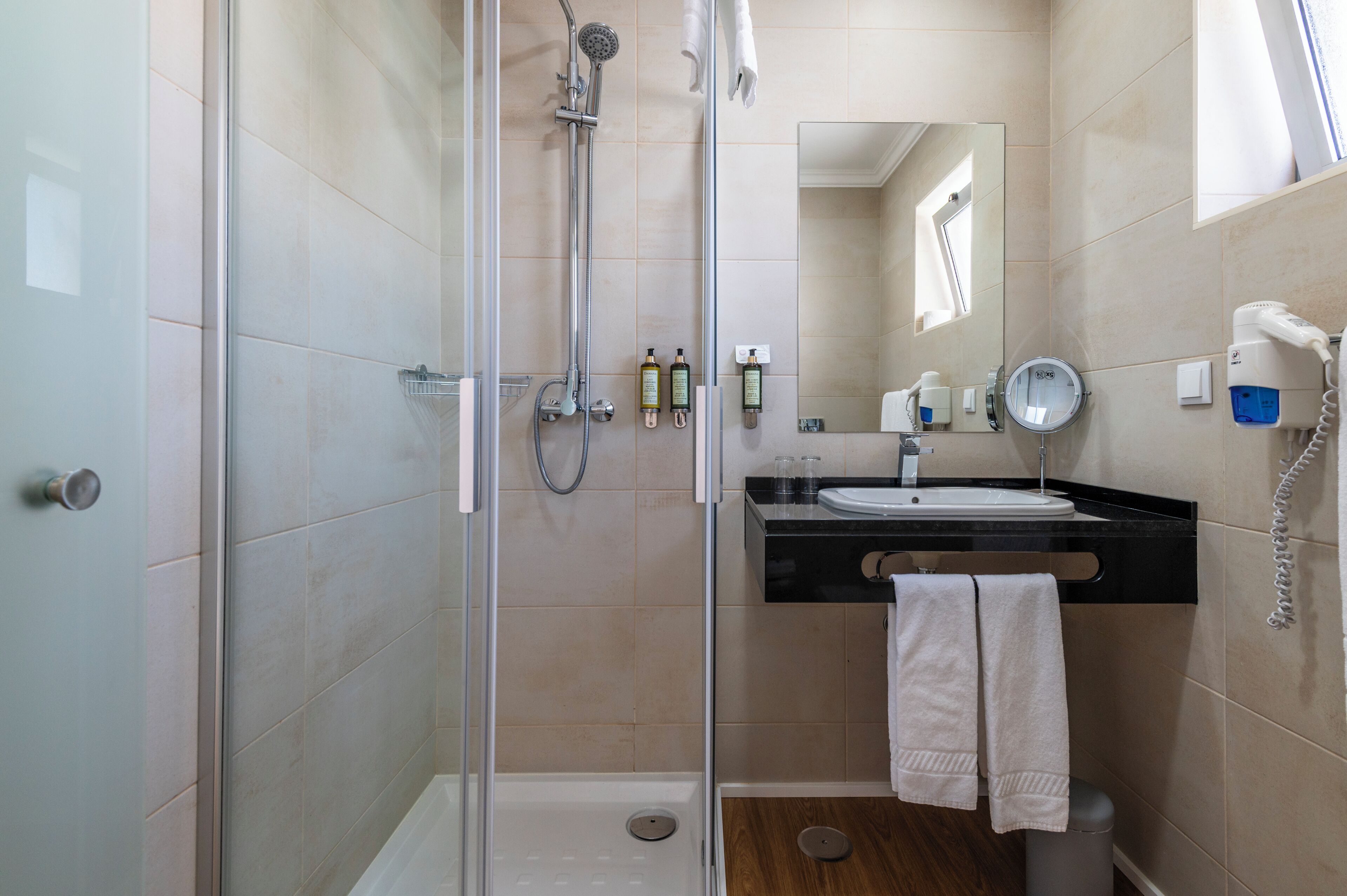 Een moderne badkamer met een douchecabine van glas, een wastafel met spiegel en toiletartikelen op het aanrecht.