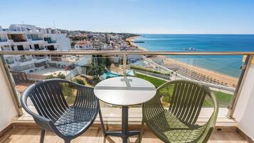 Un balcón con dos sillas y una mesa, con vista a una playa y un pueblo costero.