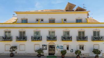 Un edificio blanco con detalles amarillos, varios balcones y plantas en macetas.