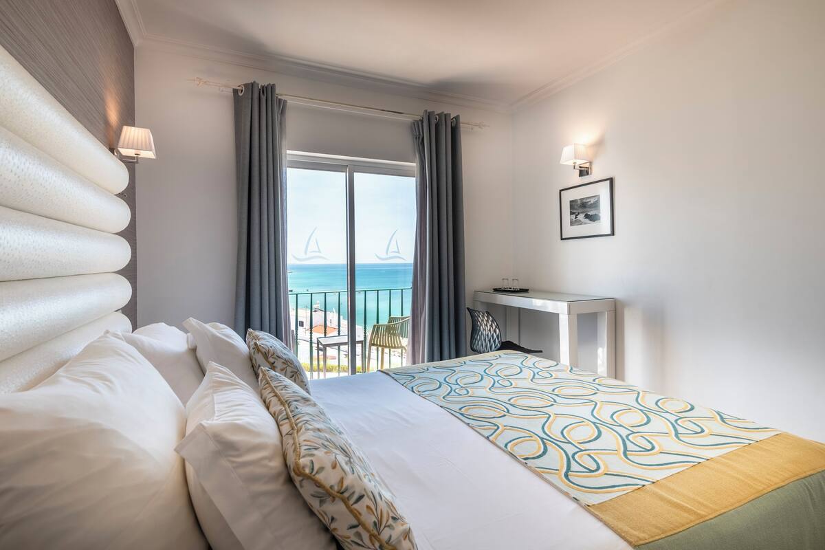 Une chambre d’hôtel avec un lit, un bureau, une chaise et une vue sur la mer.