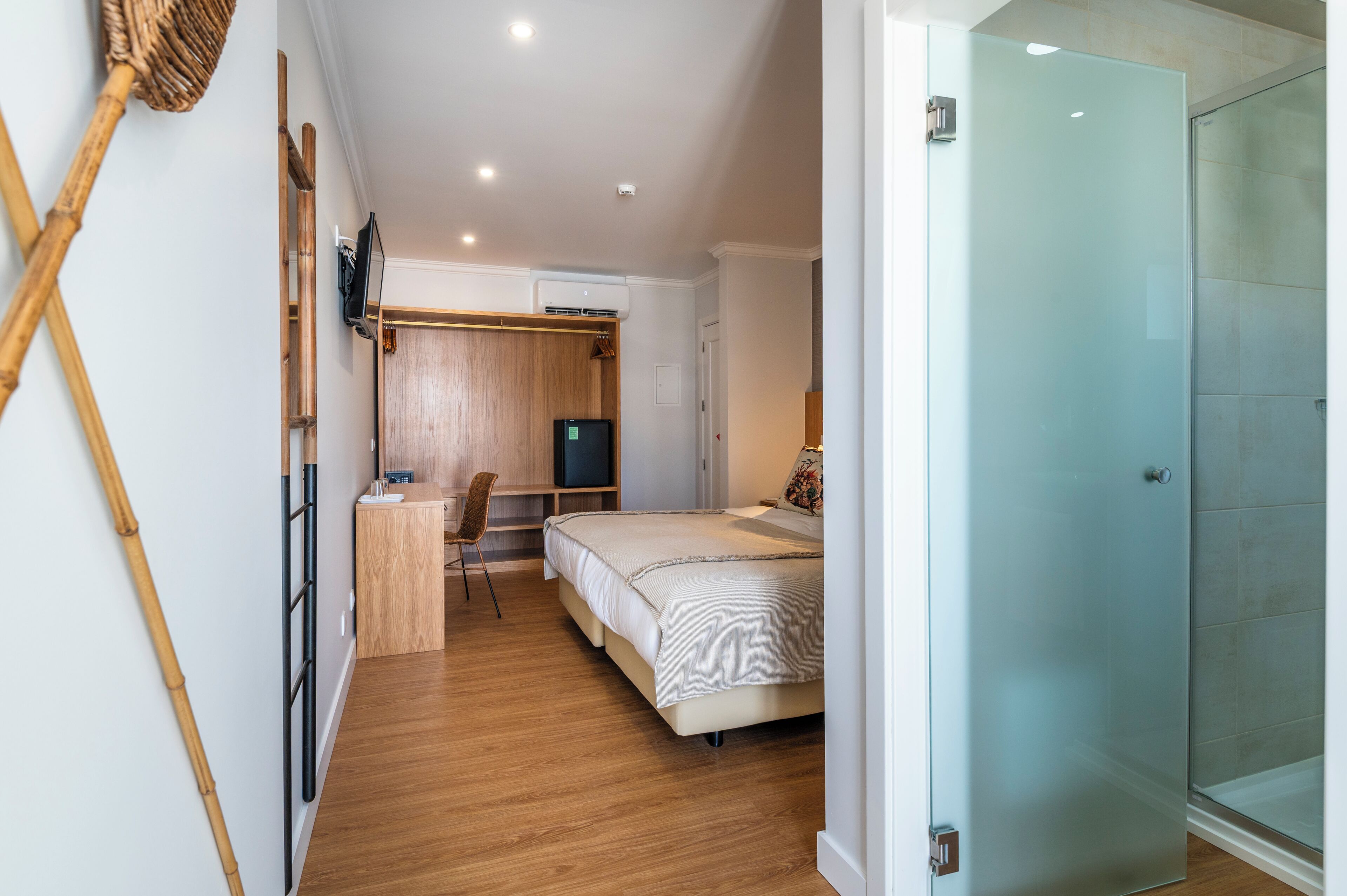 A hotel room with a bed, a desk, a chair, a television, and a glass shower door.