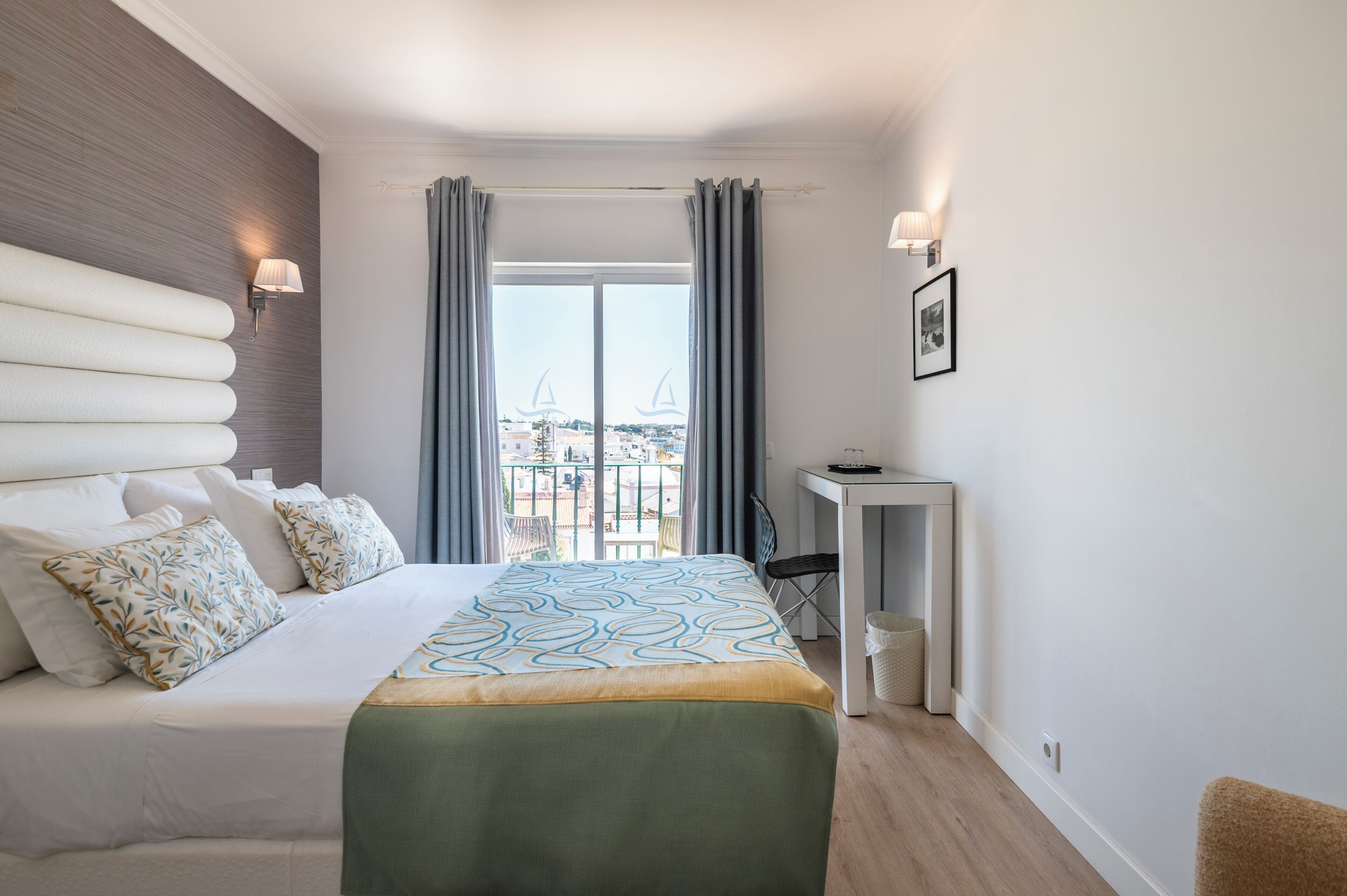 A hotel room with a bed, a desk, a chair, and a view of the city.