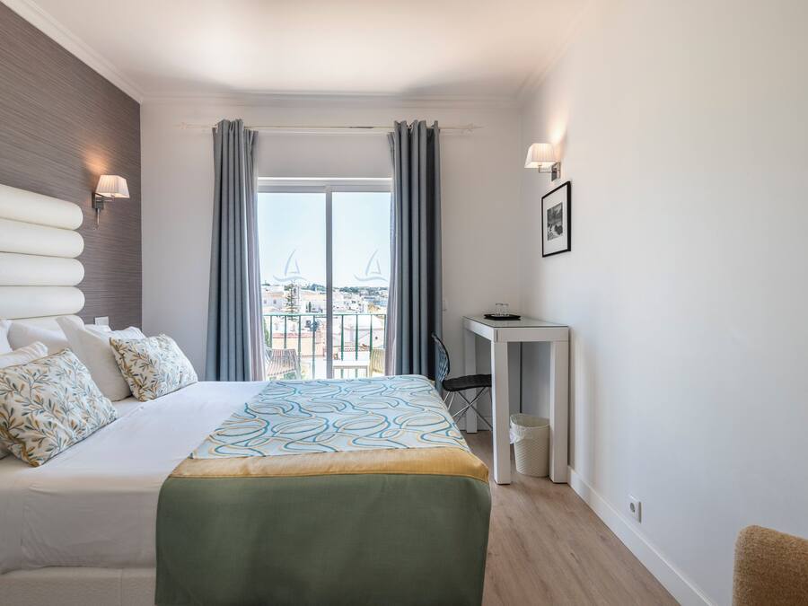 A hotel room with a bed, a desk, a chair, and a view of the city.