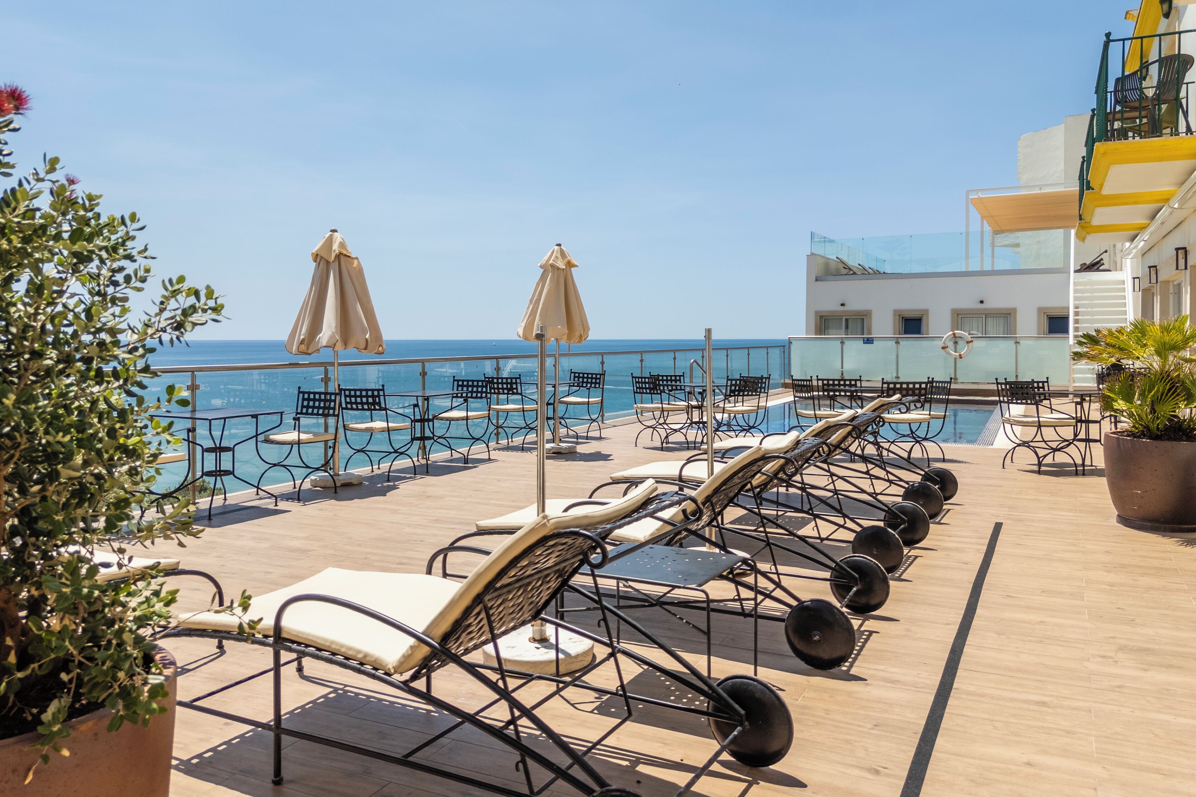 A rooftop pool area with lounge chairs and umbrellas, overlooking the sea.
