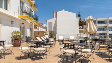 An outdoor patio with tables and chairs, a potted plant, and a building with balconies.