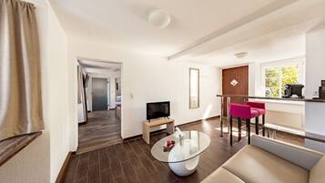 A modern living room with a glass coffee table, a flat-screen TV, a sofa, and a dining area with a bar.