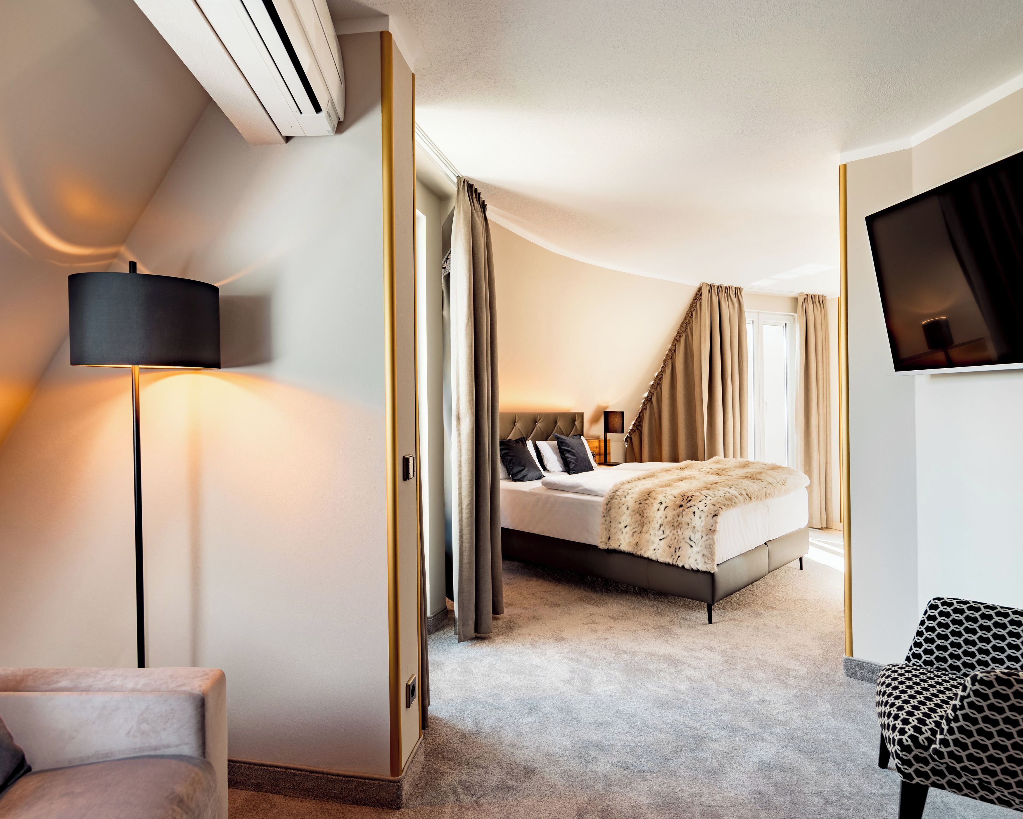 Una habitación de hotel moderna con cama, escritorio, silla, televisor y aire acondicionado.