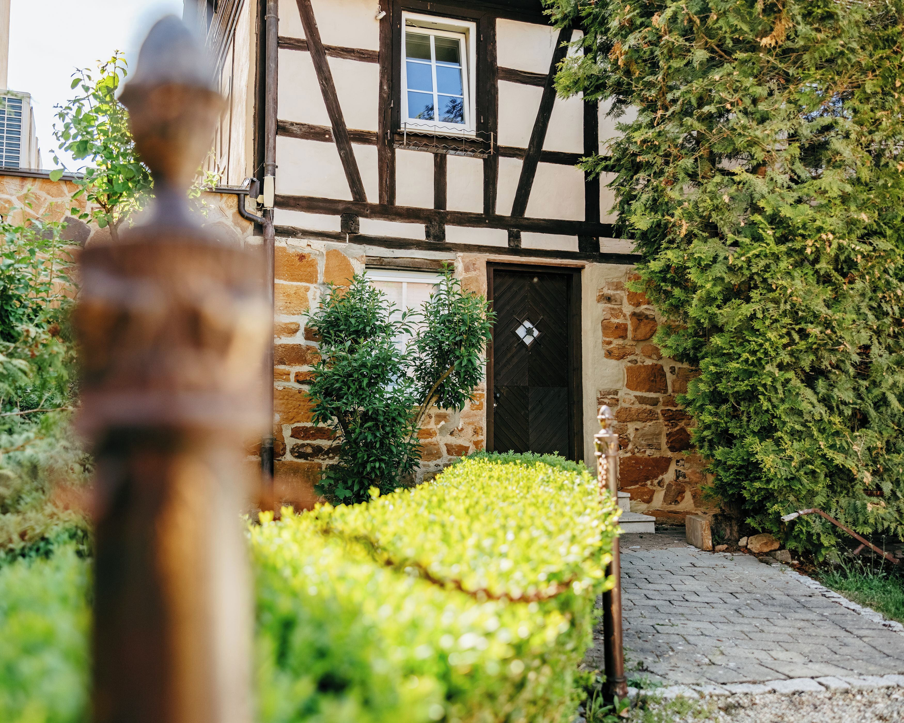 A half-timbered building with a stone wall, a door with a diamond-shaped knocker, and a small window.