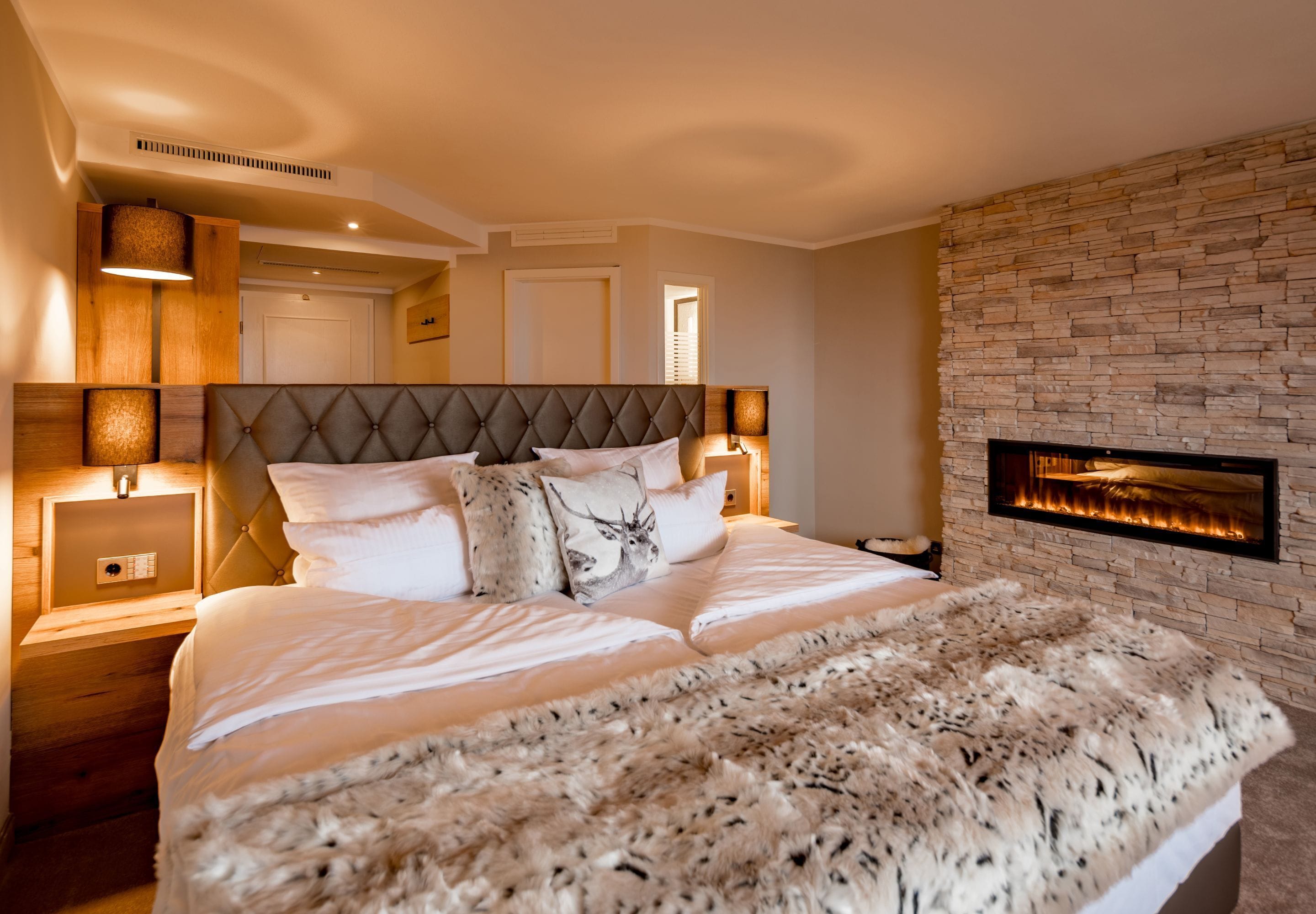 A bedroom with a large bed, a fireplace, and a stone wall.