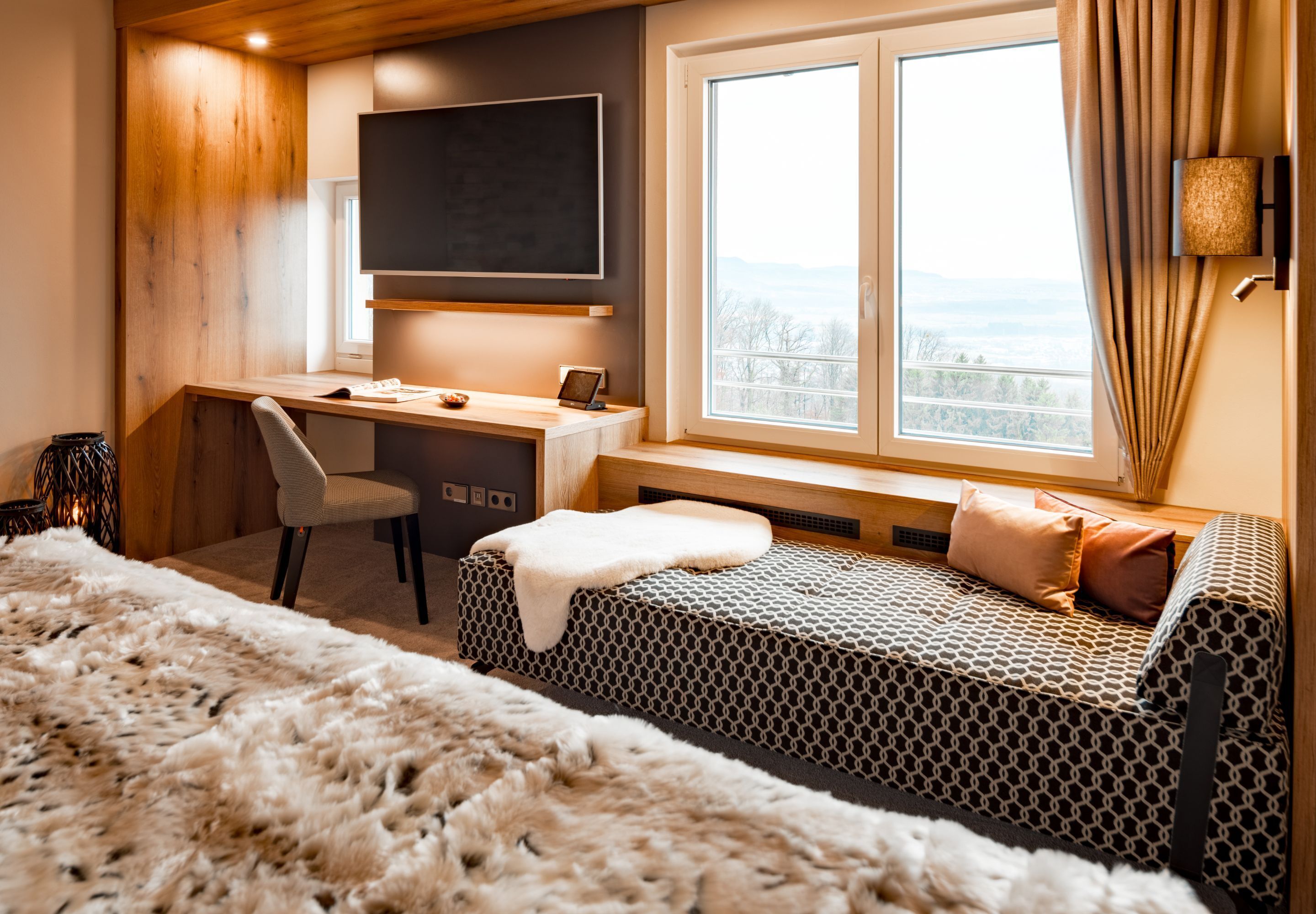 A bedroom with a desk, a chair, a bed, and a large window with a view.