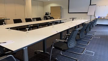 Ein Konferenzraum mit langem Tisch, Stühlen, einer Projektionsleinwand und einer Whiteboard-Tafel.