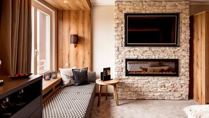 A cozy room with a stone fireplace, a bed with patterned bedding, a small round table, and a window with curtains. - Burghotel Staufeneck (Salach)