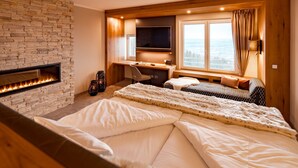 A bedroom with a stone fireplace, a desk with a computer, a bed with white bedding, and a large window with a view. - Burghotel Staufeneck (Salach)