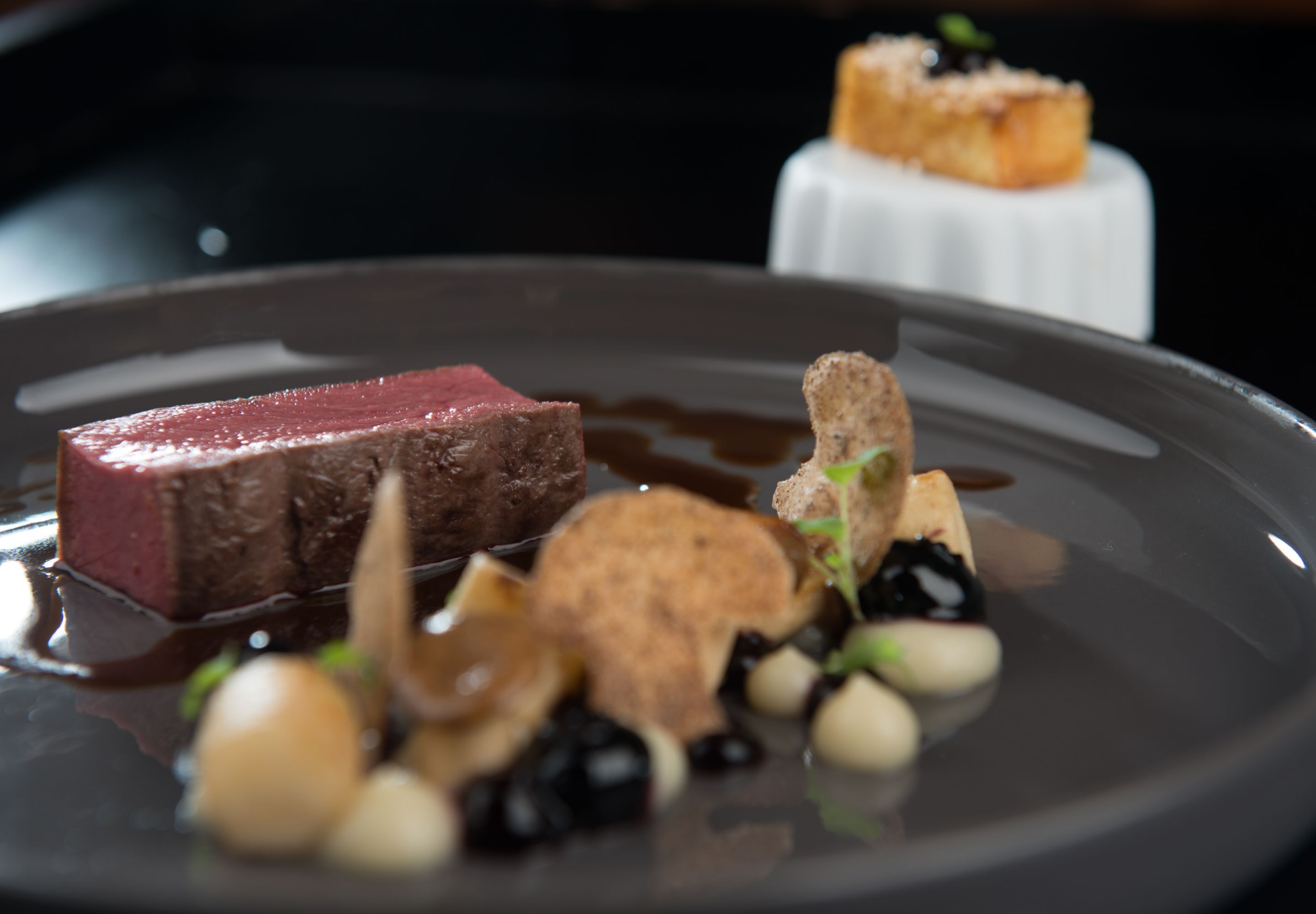 A plated dish with a piece of meat, vegetables, and a small dessert.