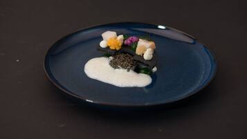 A dark blue plate with a white creamy substance, a piece of fish, and various garnishes on a dark surface.