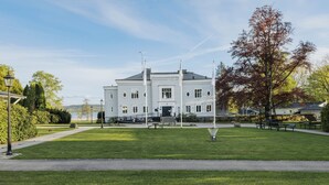 A large white building with a symmetrical facade, a central entrance, and a well-maintained lawn with benches. - Aspenäs Herrgård (Lerum)