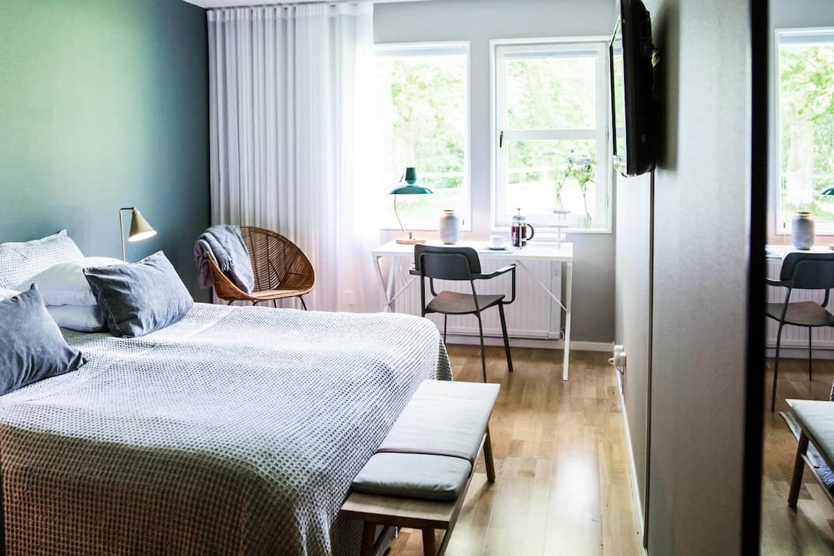A bedroom with a bed, bedside table, lamp, and a view of a dining area with chairs and a table.