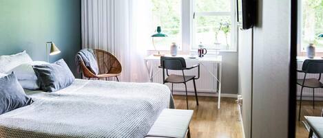Een slaapkamer met een bed, nachtkastje, lamp en uitzicht op een eetruimte met stoelen en een tafel.