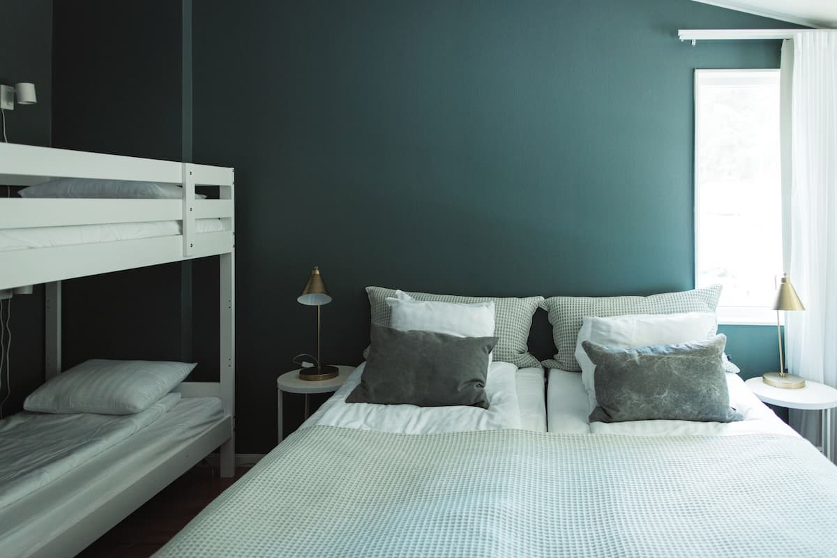 A room with a bunk bed, a single bed, and two bedside tables with lamps.