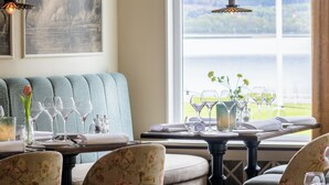 A dining area with a view of a lake, a large window, and a painting on the wall. - Aspenäs Herrgård (Lerum)