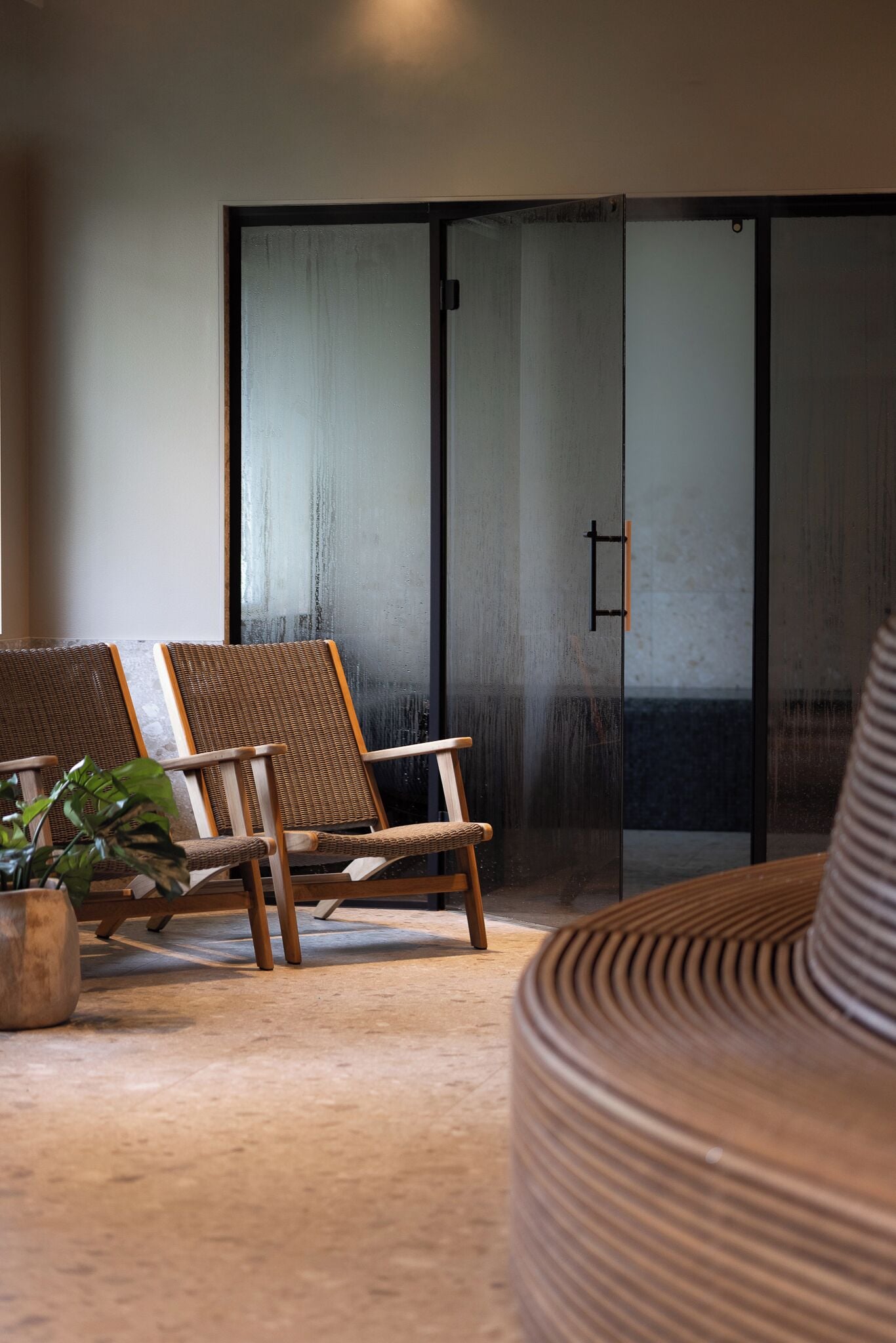 Een kamer met twee rieten stoelen, een potplant en een grote geweven fauteuil.