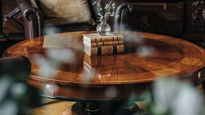 A round wooden table with a vase and books, a leather chair, and a wooden wall with carvings. - Aspenäs Herrgård (Lerum)