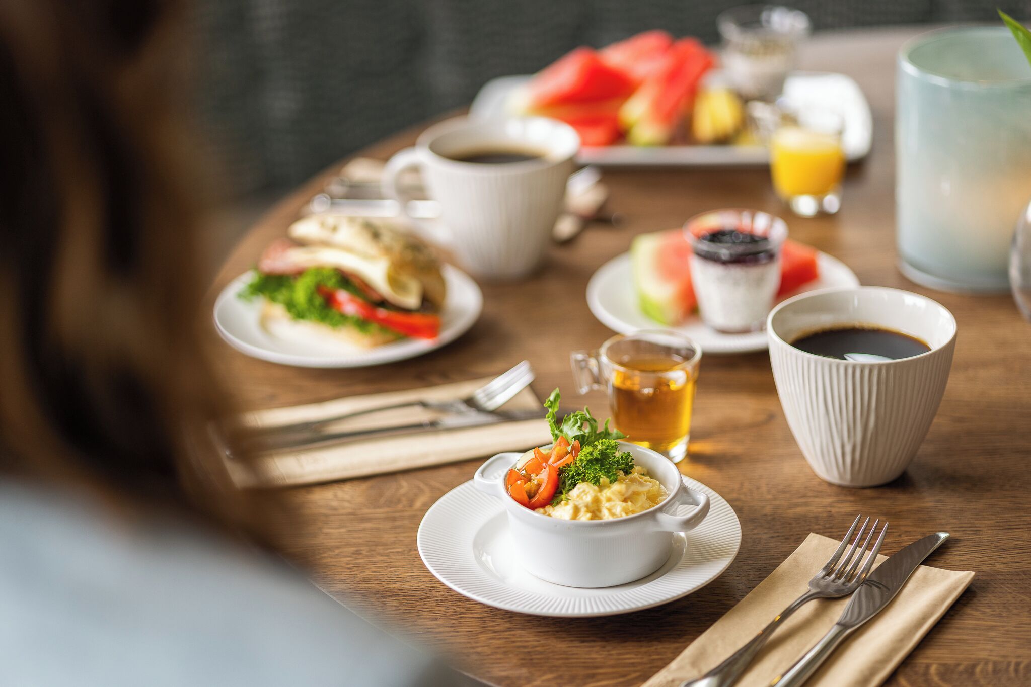 A breakfast setting with various dishes, cups, and a glass of juice on a wooden table.
