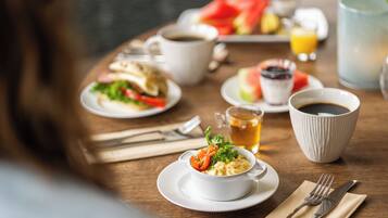 A breakfast setting with various dishes, cups, and a glass of juice on a wooden table.