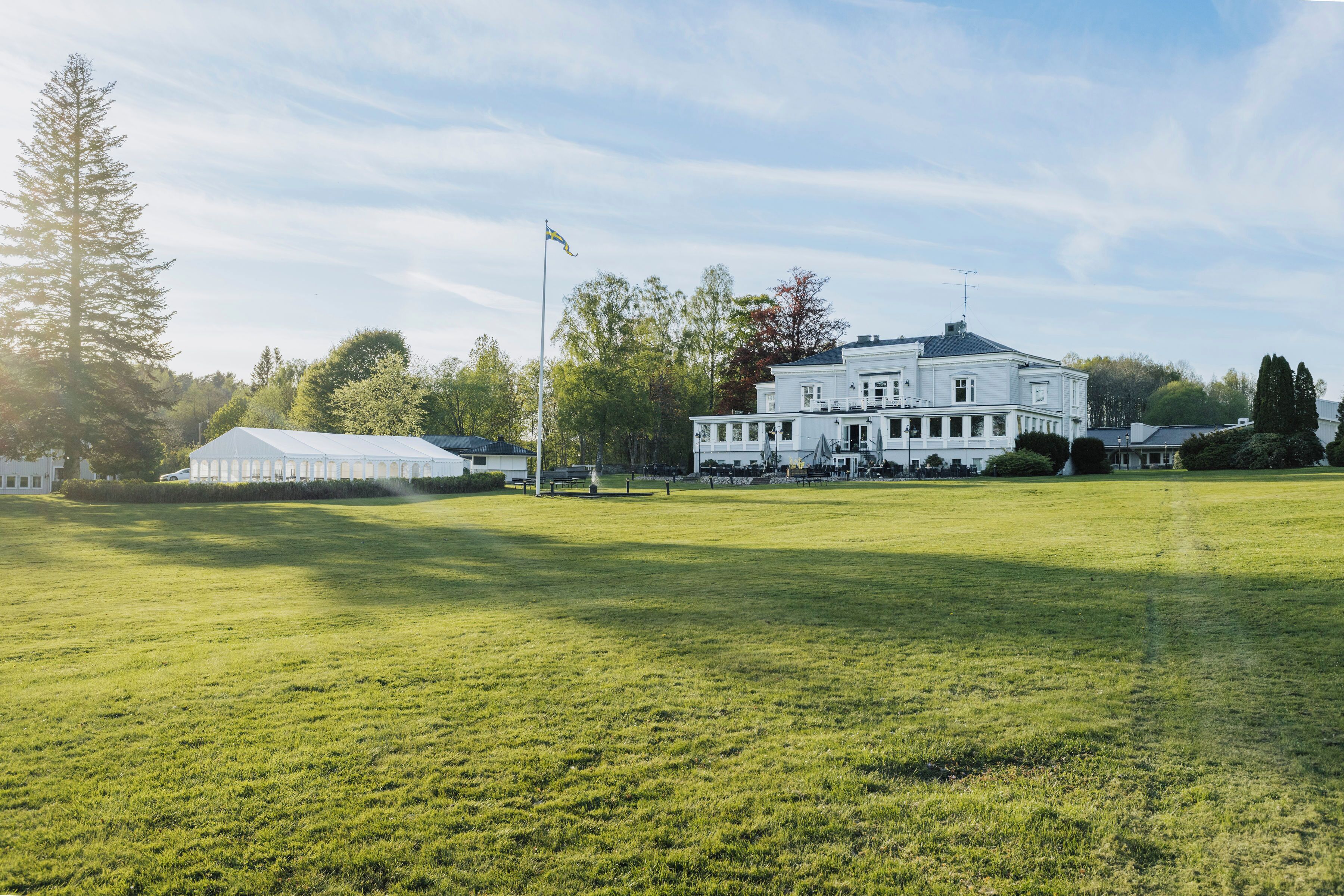 Un grand bâtiment blanc à la façade symétrique, avec un mât et une pelouse bien entretenue.