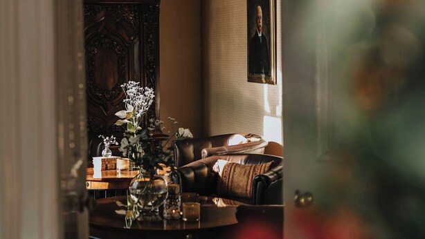 A room with a chandelier, a fireplace, a framed portrait, and a leather sofa. - Aspenäs Herrgård (Lerum)