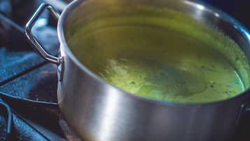 Una persona vertiendo un líquido verde de una cuchara sopera en un tazón con algo crujiente encima.